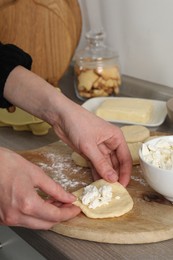 Photo of Woman making pirozhki (stuffed pastry pies) with cottage cheese at countertop indoors, closeup