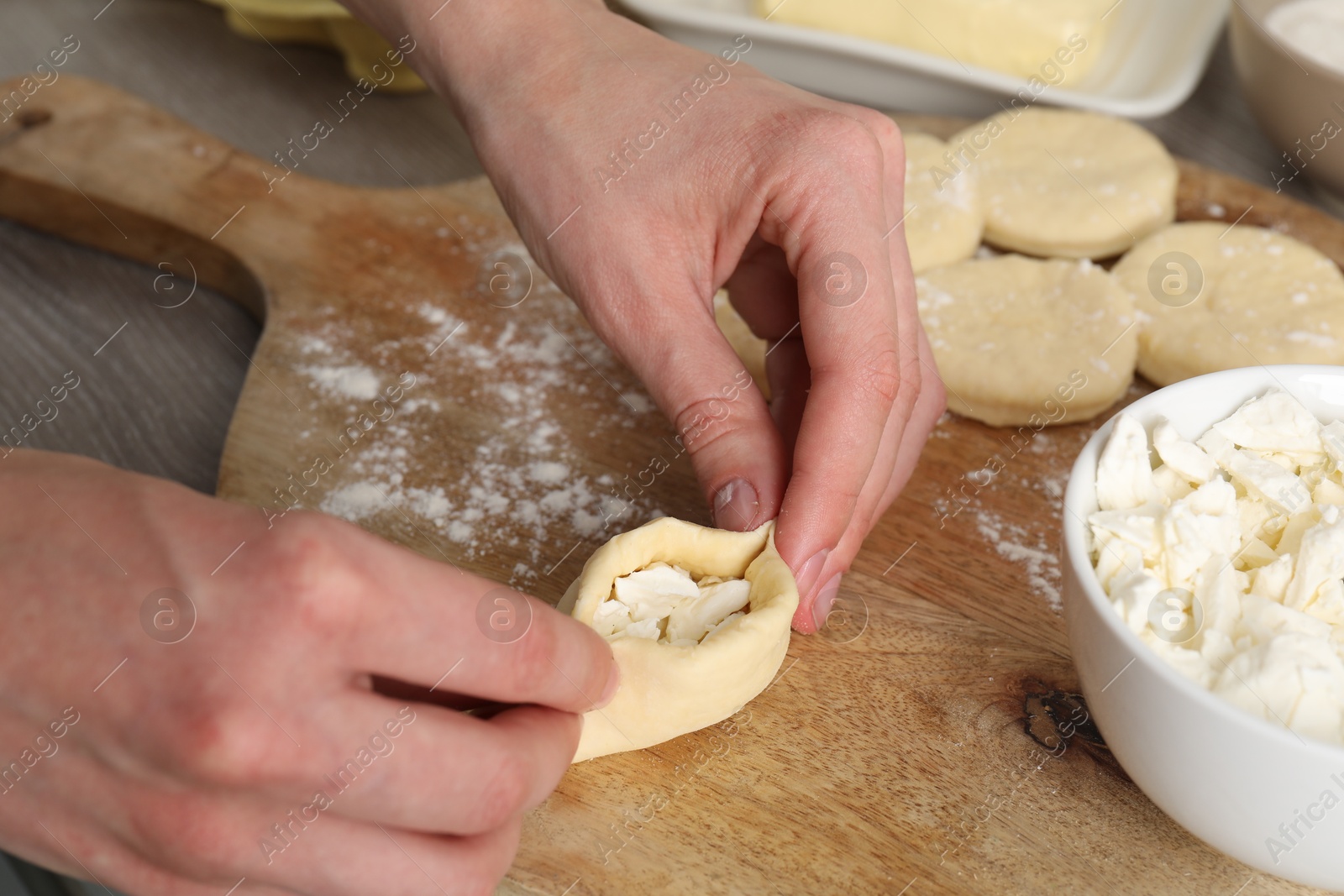 Photo of Woman making pirozhki (stuffed pastry pies) with cottage cheese at table, closeup