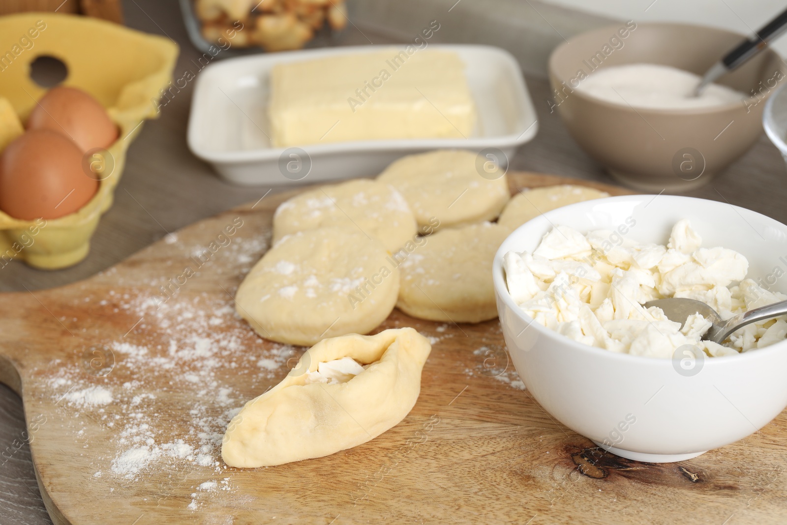 Photo of Making pirozhki (stuffed pastry pies). Pieces of dough with cottage cheese on wooden table, closeup