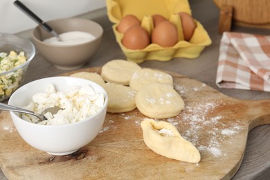 Photo of Making pirozhki (stuffed pastry pies). Pieces of dough with cottage cheese on wooden table, closeup