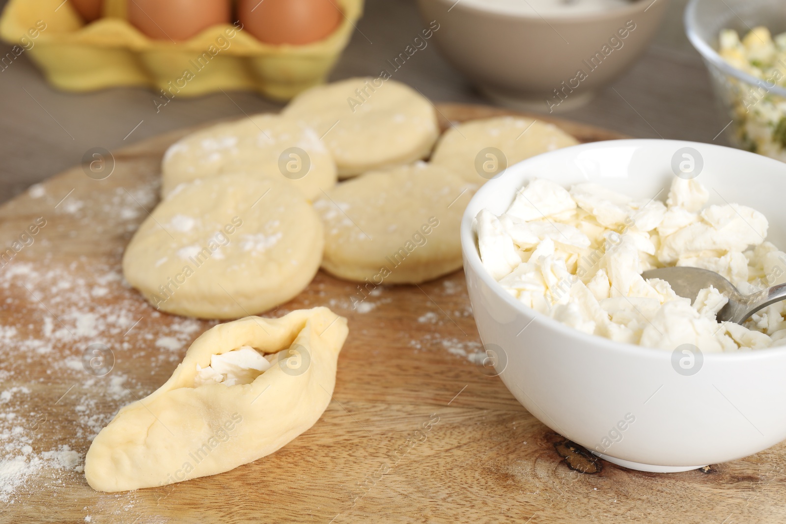 Photo of Making pirozhki (stuffed pastry pies). Pieces of dough with cottage cheese on wooden table, closeup