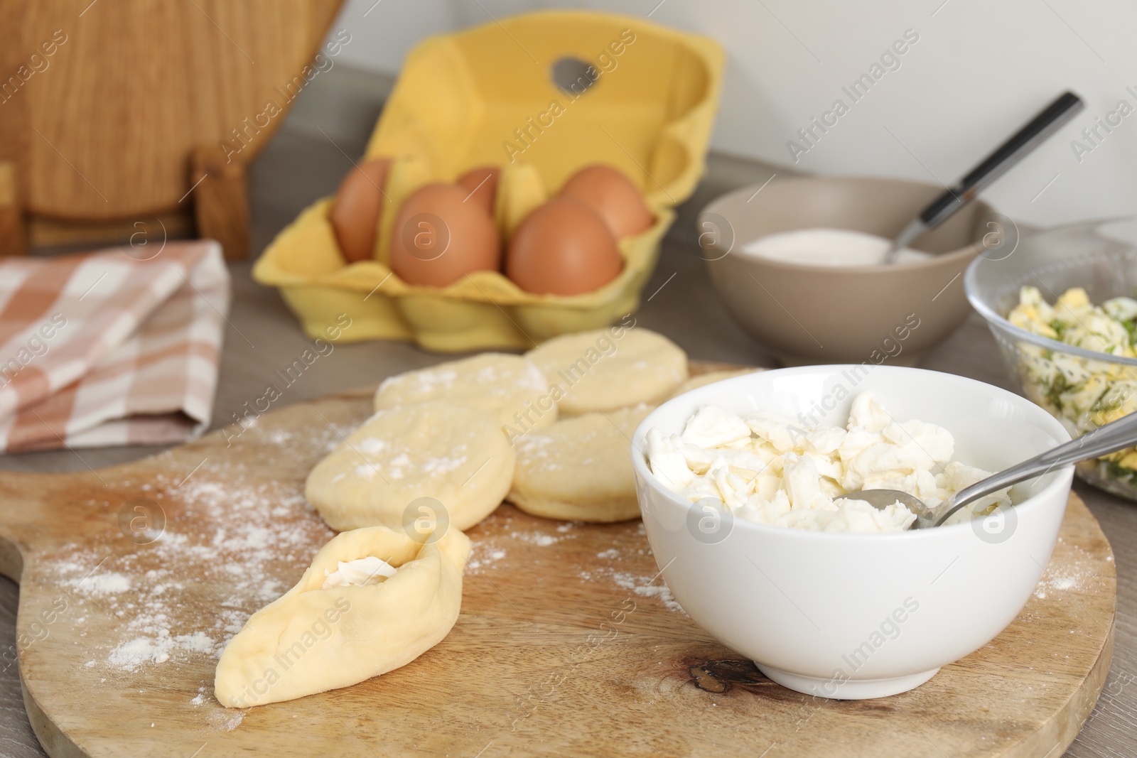 Photo of Making pirozhki (stuffed pastry pies). Pieces of dough with cottage cheese on table, closeup