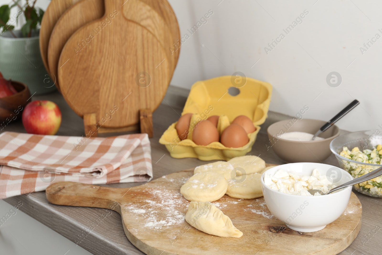 Photo of Making pirozhki (stuffed pastry pies). Pieces of dough with cottage cheese on wooden countertop, closeup