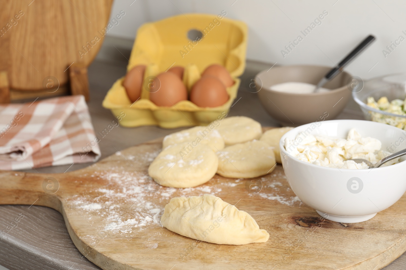 Photo of Making pirozhki (stuffed pastry pies). Pieces of dough with cottage cheese on wooden countertop, closeup