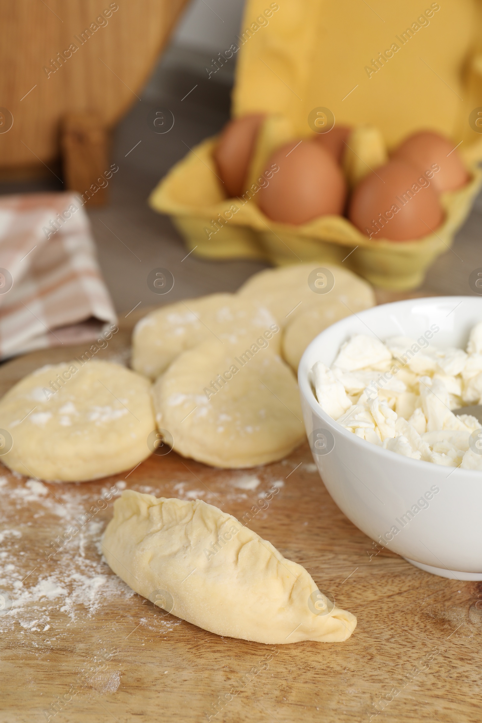 Photo of Making pirozhki (stuffed pastry pies). Pieces of dough with cottage cheese on table, closeup