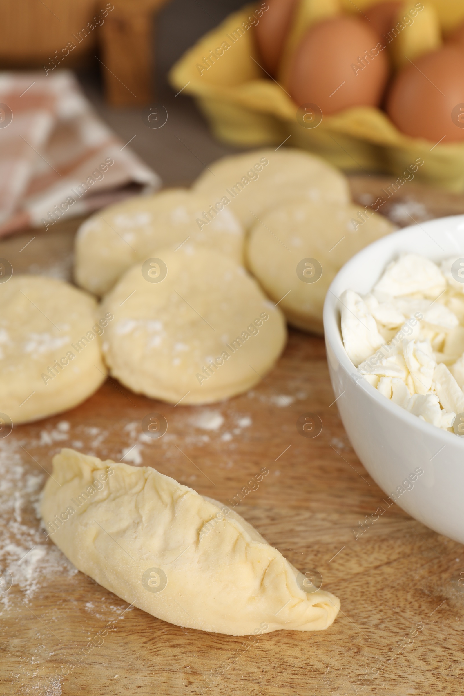 Photo of Making pirozhki (stuffed pastry pies). Pieces of dough with cottage cheese on wooden table, closeup