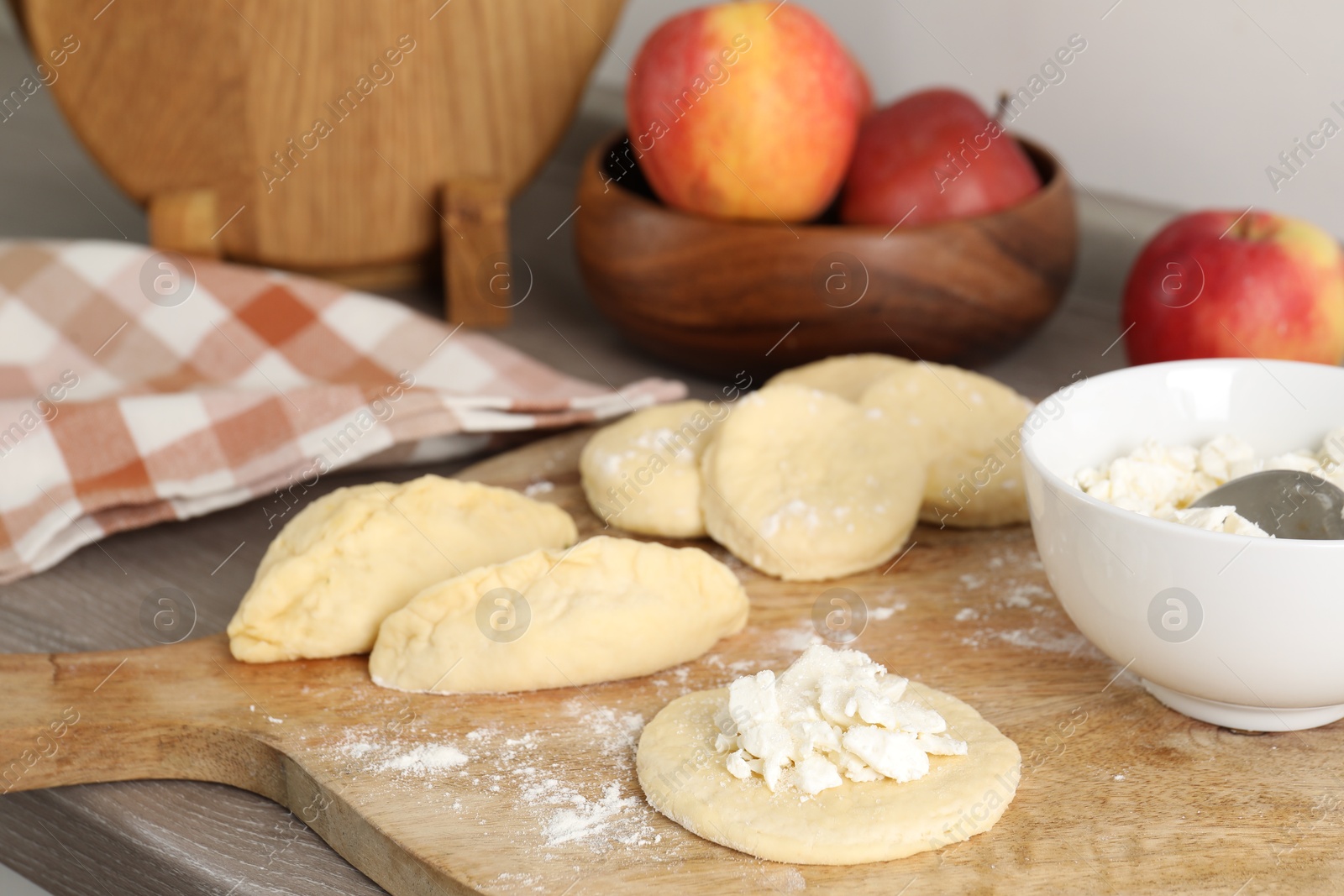 Photo of Making pirozhki (stuffed pastry pies). Pieces of dough with cottage cheese on wooden countertop, closeup