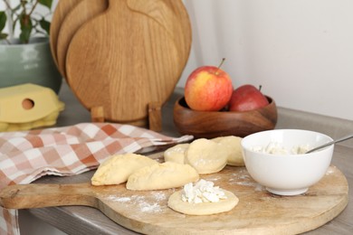 Photo of Making pirozhki (stuffed pastry pies). Pieces of dough with cottage cheese on wooden countertop, closeup