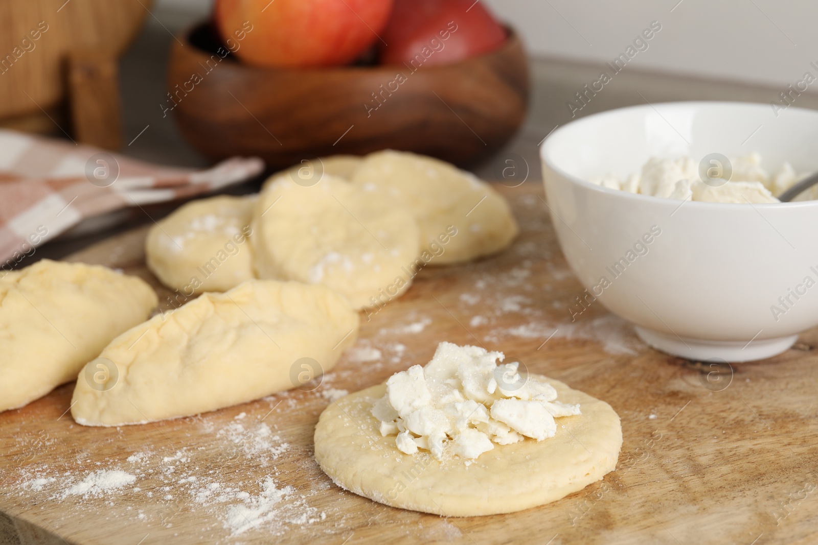 Photo of Making pirozhki (stuffed pastry pies). Pieces of dough with cottage cheese on wooden table, closeup