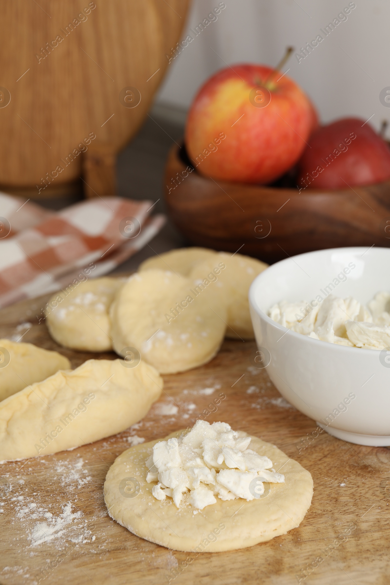 Photo of Making pirozhki (stuffed pastry pies). Pieces of dough with cottage cheese on wooden table, closeup