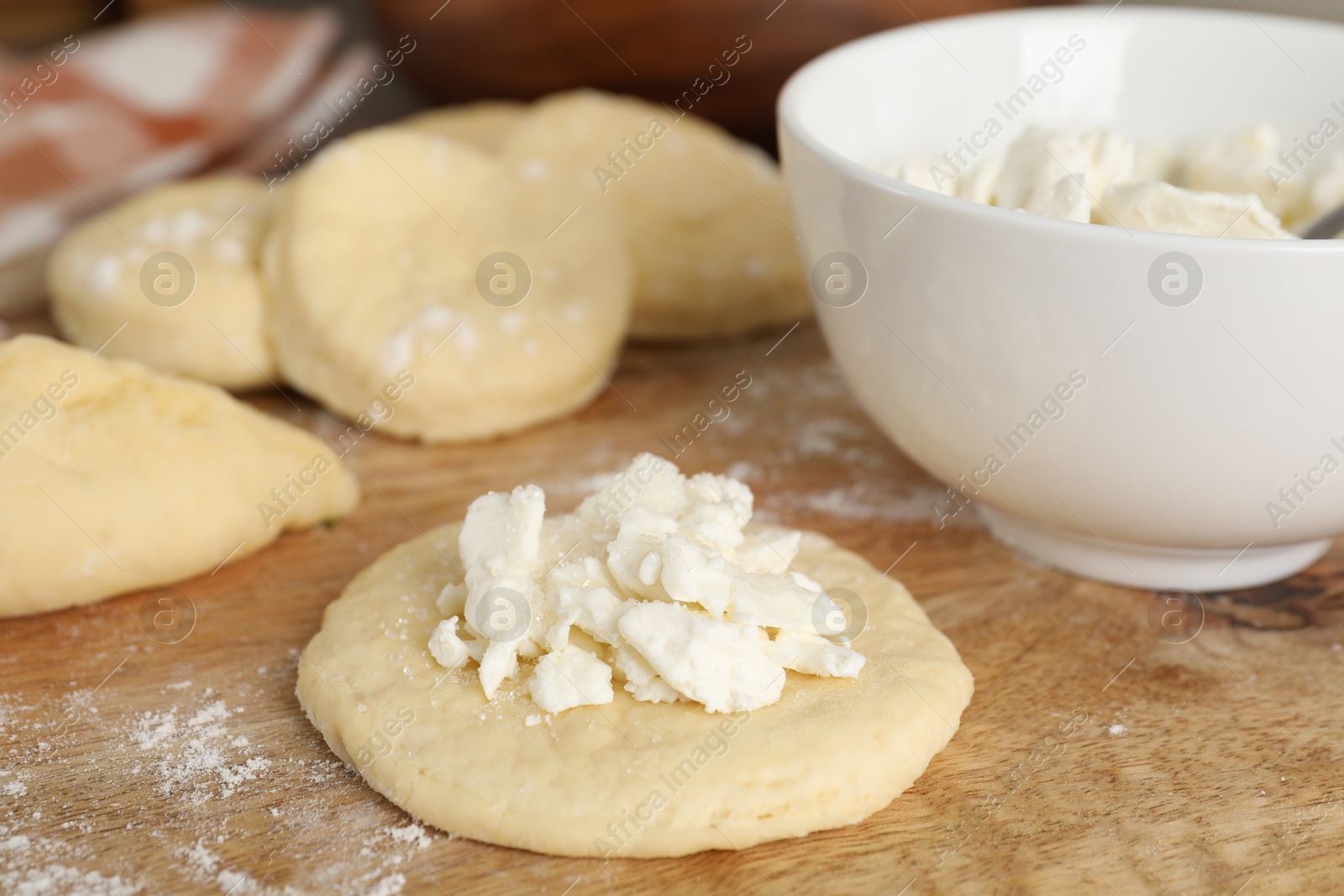 Photo of Making pirozhki (stuffed pastry pies). Pieces of dough with cottage cheese on wooden table, closeup