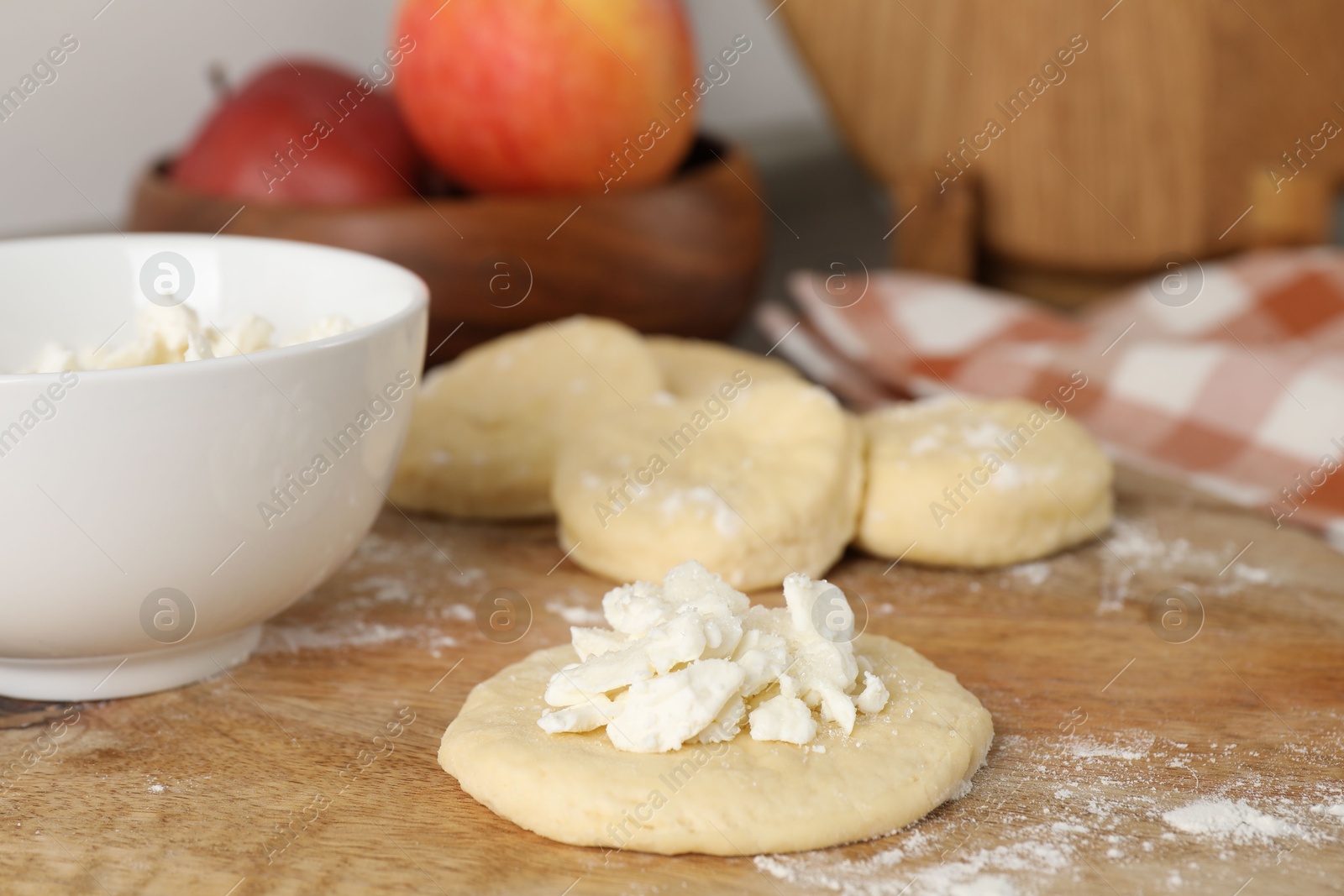 Photo of Making pirozhki (stuffed pastry pies). Pieces of dough with cottage cheese on wooden table, closeup