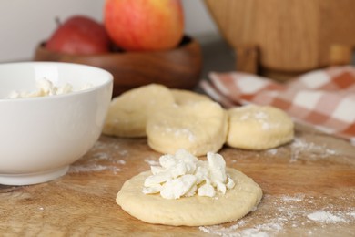 Photo of Making pirozhki (stuffed pastry pies). Pieces of dough with cottage cheese on wooden table, closeup