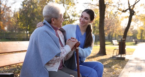 Photo of Elderly woman with walking cane and her caregiver in park