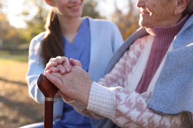 Photo of Elderly woman with walking cane and her caregiver in park, closeup