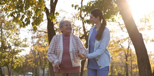 Photo of Elderly woman with walking cane and her caregiver in park