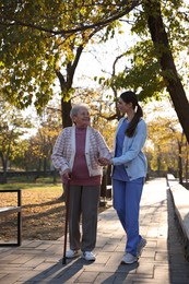 Photo of Elderly woman with walking cane and her caregiver in park