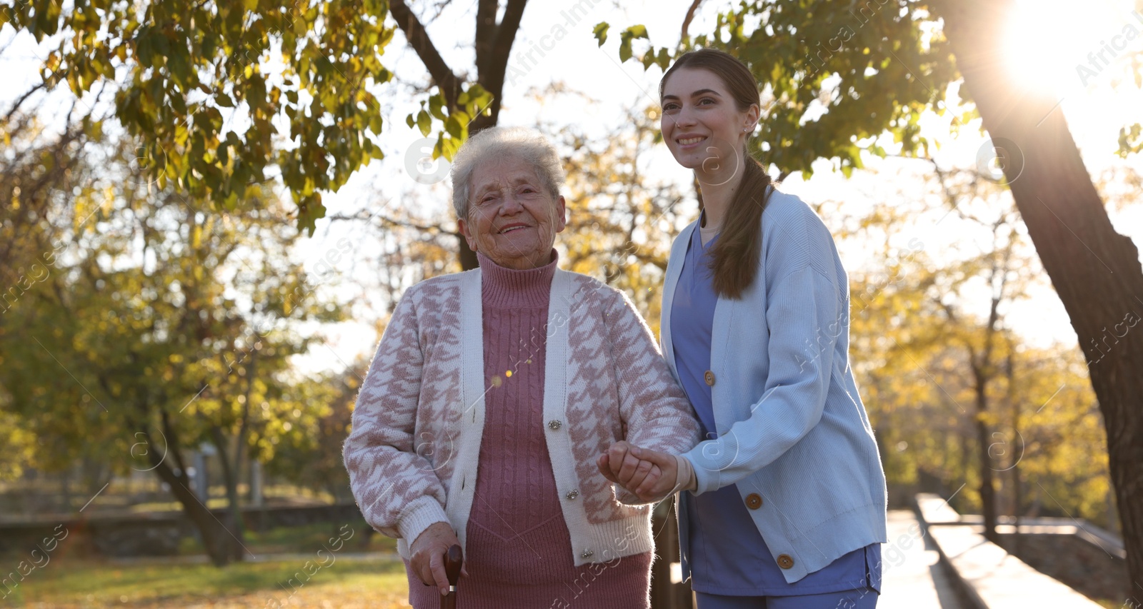 Photo of Elderly woman with walking cane and her caregiver in park