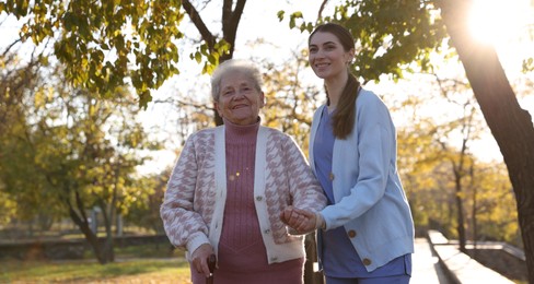 Photo of Elderly woman with walking cane and her caregiver in park