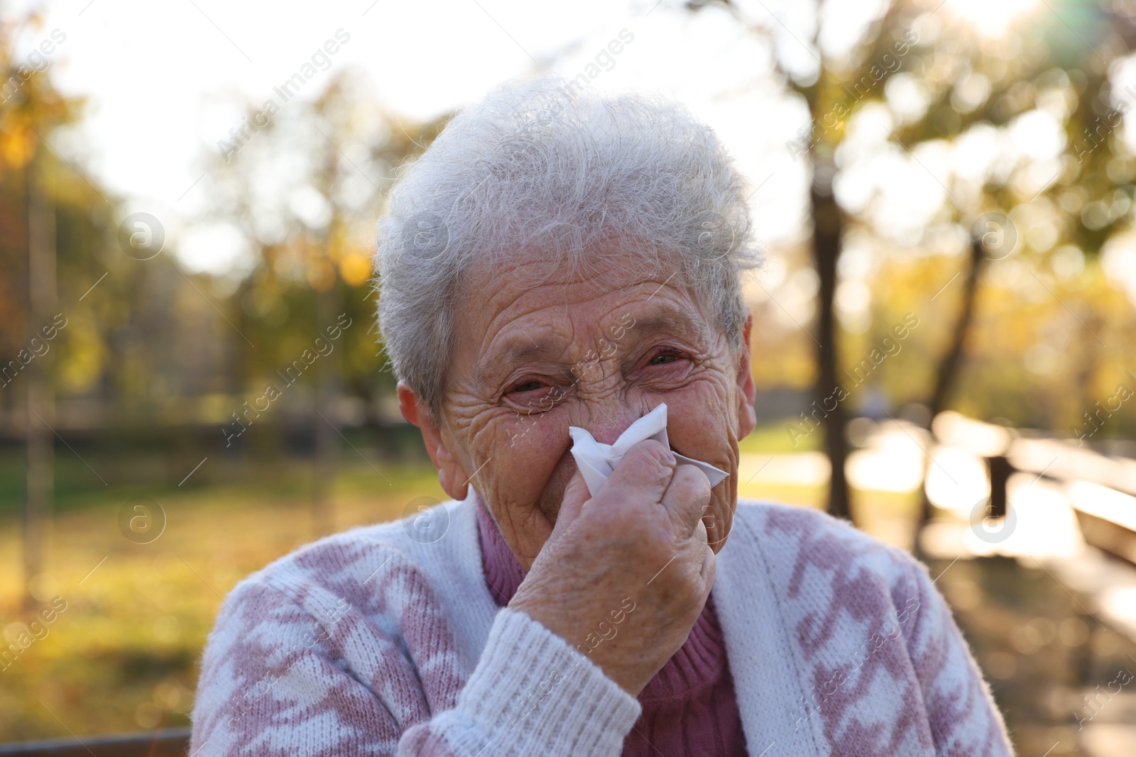 Photo of Senior woman with tissue blowing runny nose in park