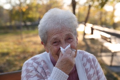 Photo of Senior woman with tissue blowing runny nose in park