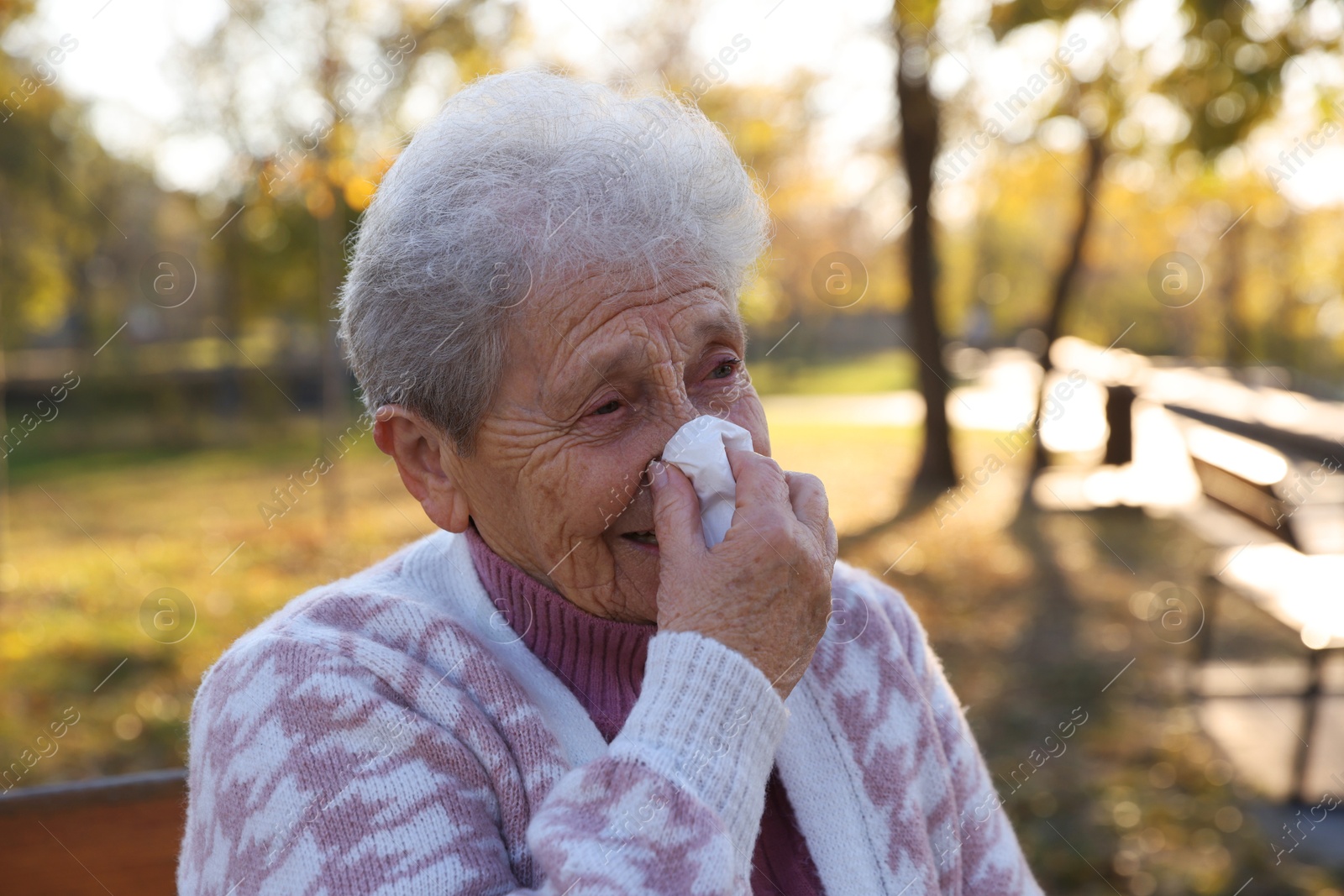 Photo of Senior woman with tissue blowing runny nose in park