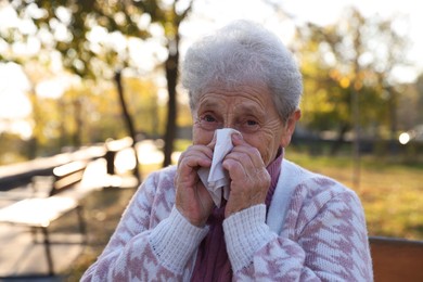 Photo of Senior woman with tissue blowing runny nose in park