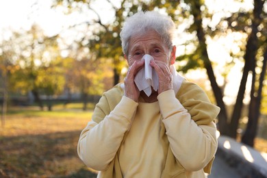 Photo of Senior woman with tissue blowing runny nose in park