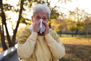 Photo of Senior woman with tissue blowing runny nose in park