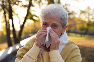 Photo of Senior woman with tissue blowing runny nose in park