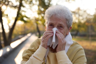 Photo of Senior woman with tissue blowing runny nose in park