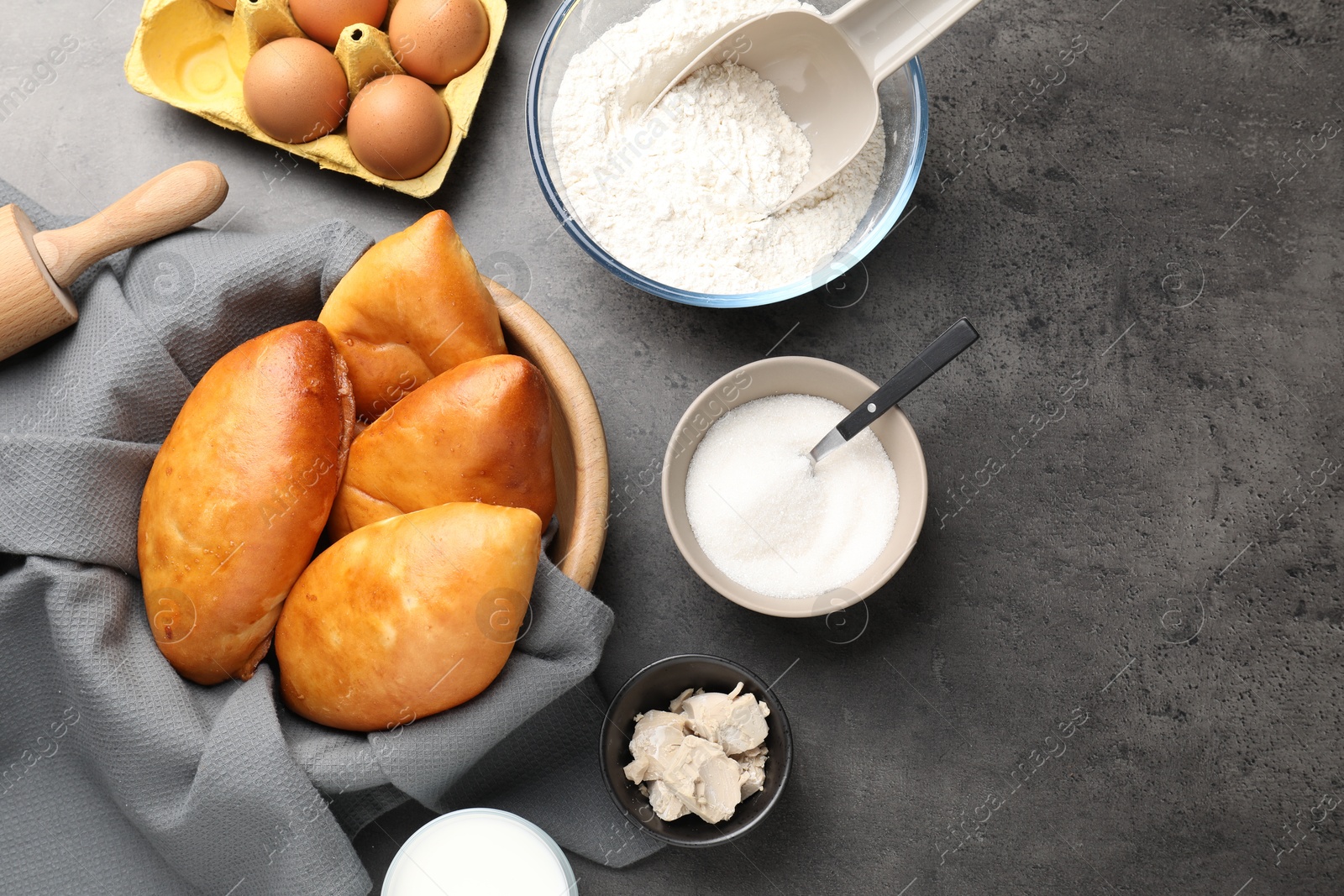 Photo of Delicious pirozhki (stuffed pastry pies) and ingredients on grey table, flat lay