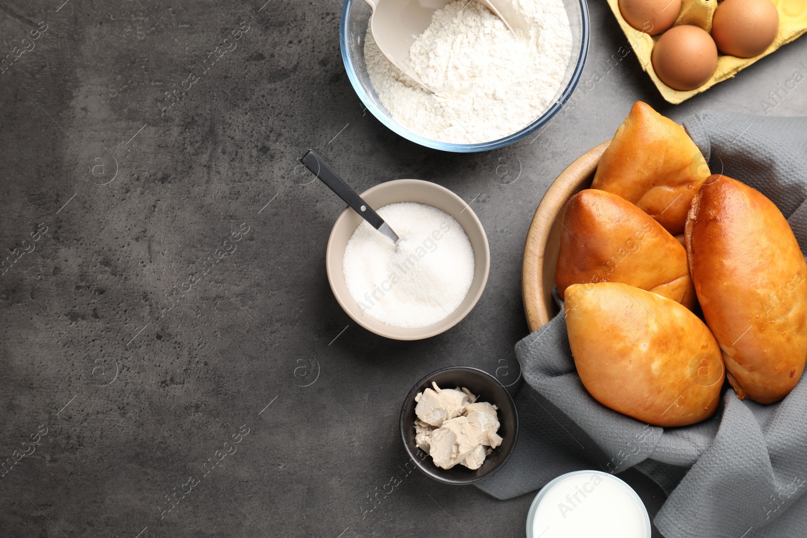 Photo of Delicious pirozhki (stuffed pastry pies) and ingredients on grey table, flat lay. Space for text