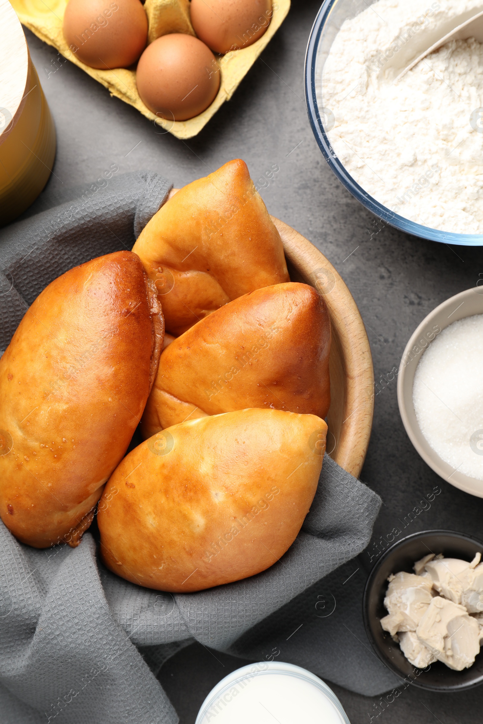 Photo of Delicious pirozhki (stuffed pastry pies) and ingredients on grey table, flat lay