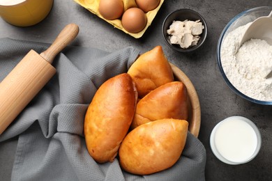 Photo of Delicious pirozhki (stuffed pastry pies) and ingredients on grey table, flat lay