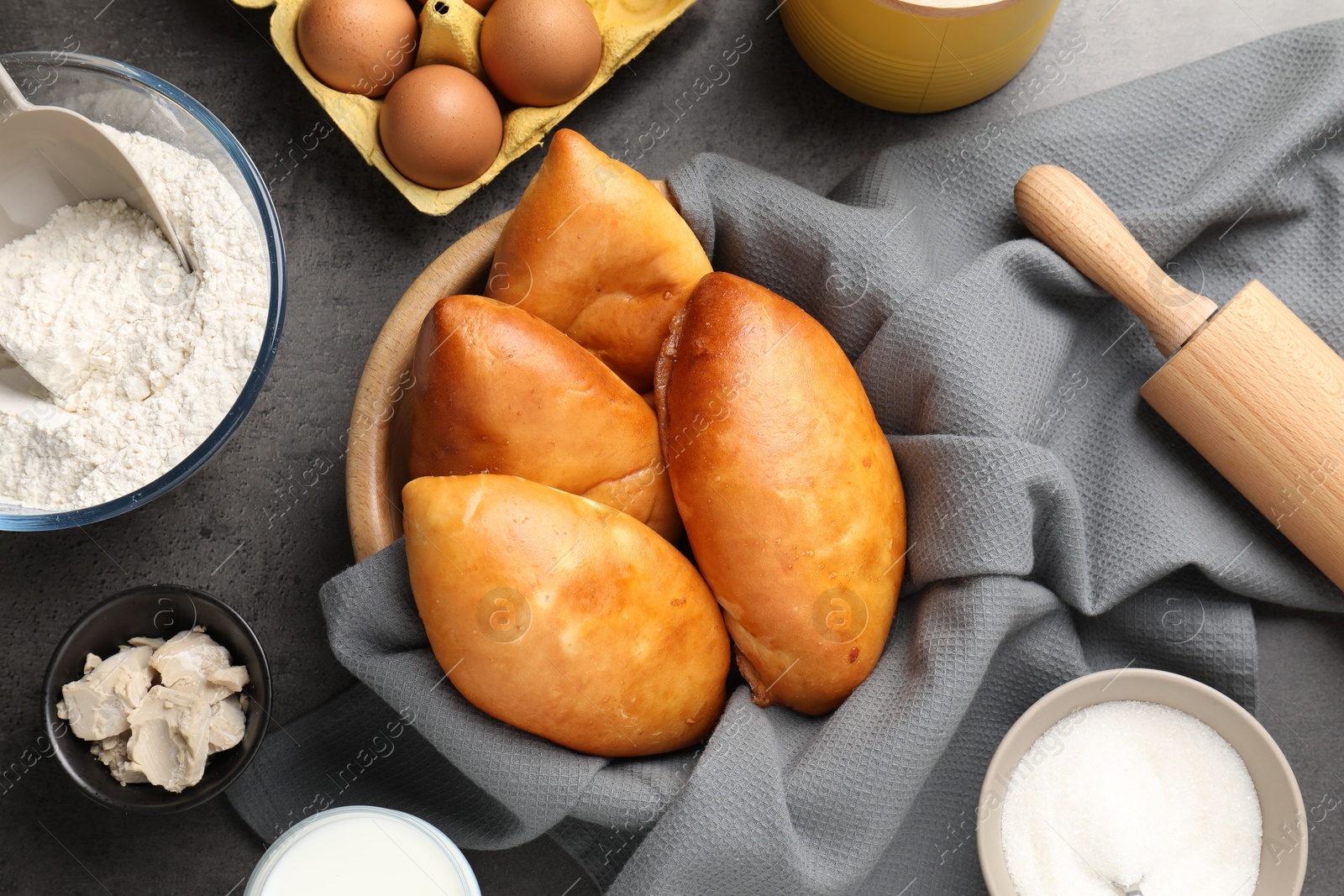 Photo of Delicious pirozhki (stuffed pastry pies) and ingredients on grey table, flat lay