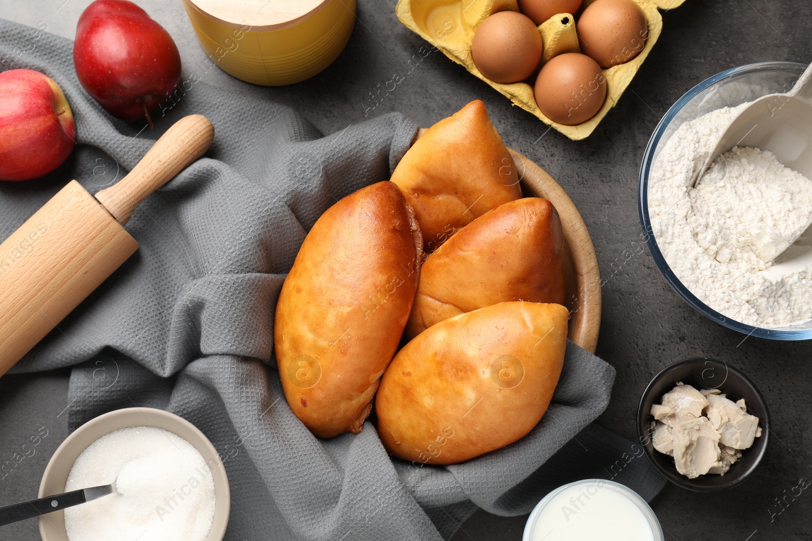 Photo of Delicious pirozhki (stuffed pastry pies) and ingredients on grey table, flat lay