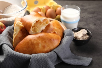 Photo of Delicious pirozhki (stuffed pastry pies) with apples and ingredients on grey table, closeup