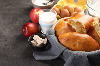 Photo of Delicious pirozhki (stuffed pastry pies) with apples and ingredients on grey table, closeup