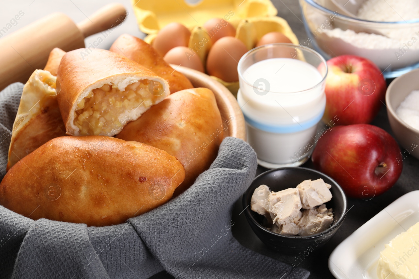 Photo of Delicious pirozhki (stuffed pastry pies) with apples and ingredients on table, closeup