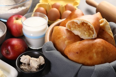 Photo of Delicious pirozhki (stuffed pastry pies) with apples and ingredients on table, closeup