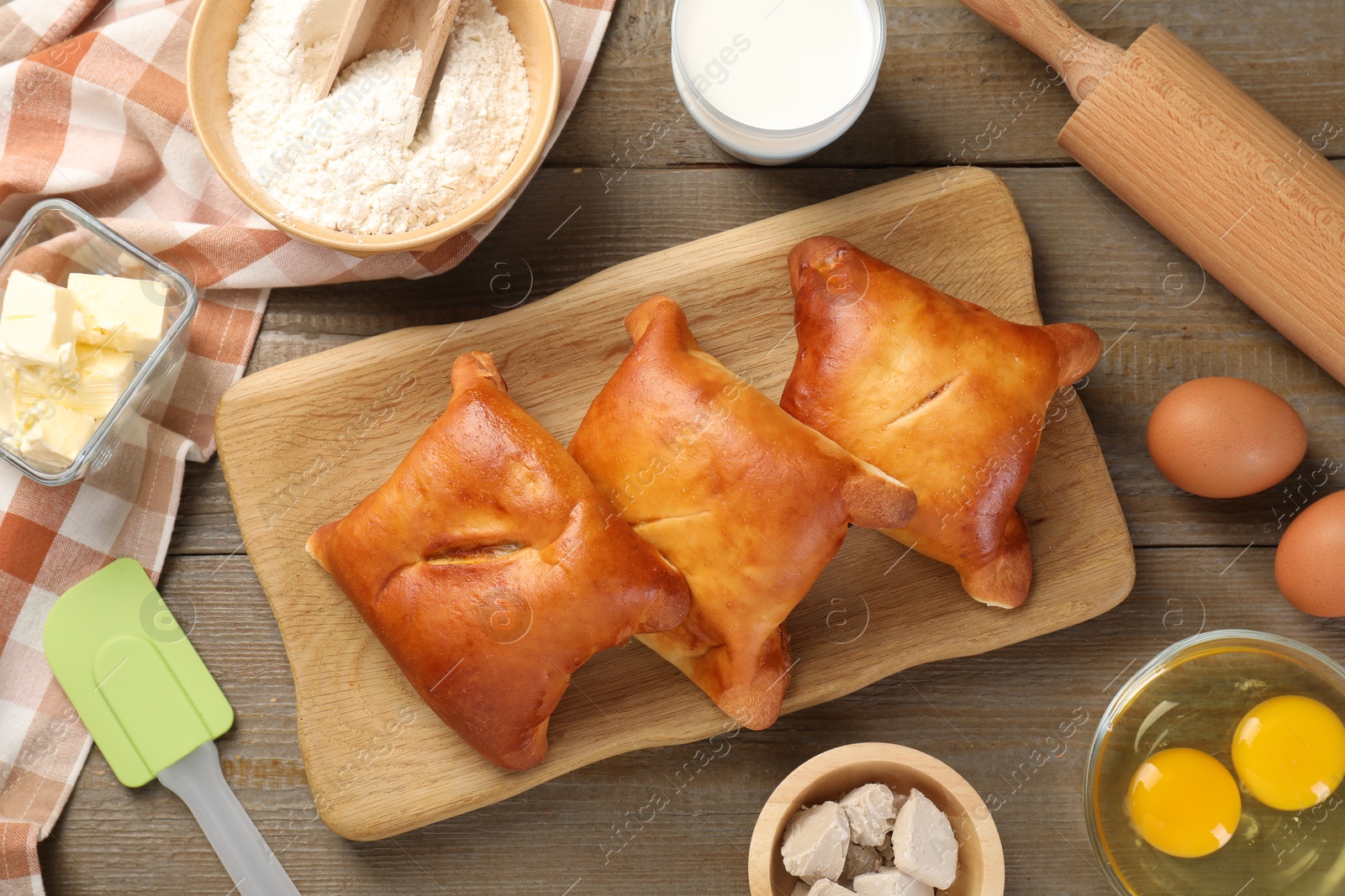 Photo of Delicious pirozhki (stuffed pastry pies) and ingredients on wooden table, flat lay