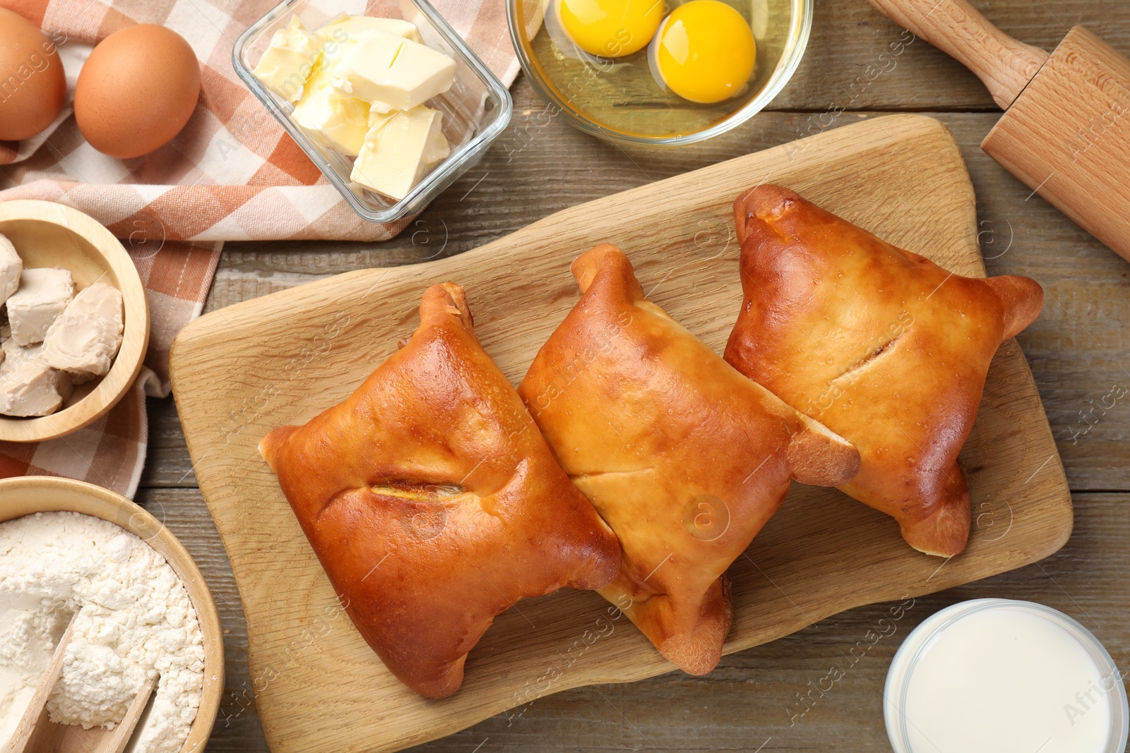 Photo of Delicious pirozhki (stuffed pastry pies) and ingredients on wooden table, flat lay