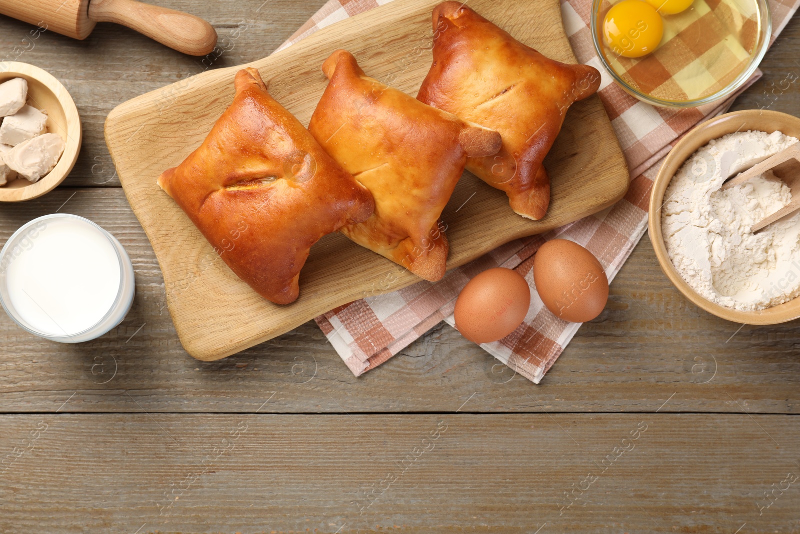 Photo of Delicious pirozhki (stuffed pastry pies) and ingredients on wooden table, flat lay. Space for text