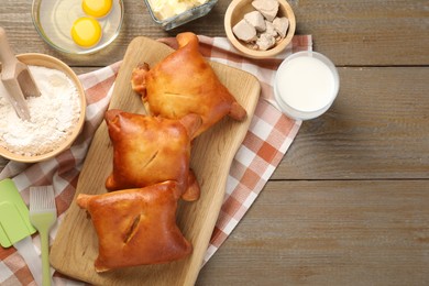 Photo of Delicious pirozhki (stuffed pastry pies) and ingredients on wooden table, flat lay. Space for text