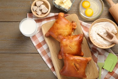 Photo of Delicious pirozhki (stuffed pastry pies) and ingredients on wooden table, flat lay