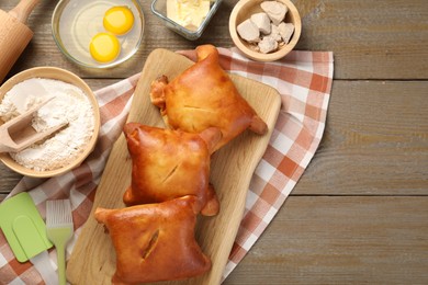 Photo of Delicious pirozhki (stuffed pastry pies) and ingredients on wooden table, flat lay