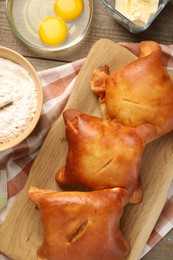 Photo of Delicious pirozhki (stuffed pastry pies) and ingredients on wooden table, flat lay