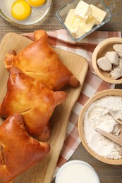 Photo of Delicious pirozhki (stuffed pastry pies) and ingredients on wooden table, flat lay