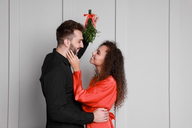 Photo of Lovely couple under mistletoe bunch near light grey wall